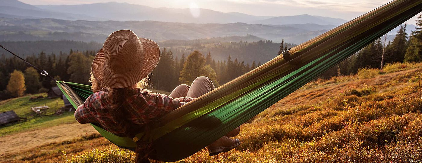 Woman with a hat relaxing in a hammock overlooking an autumn mountain landscape.